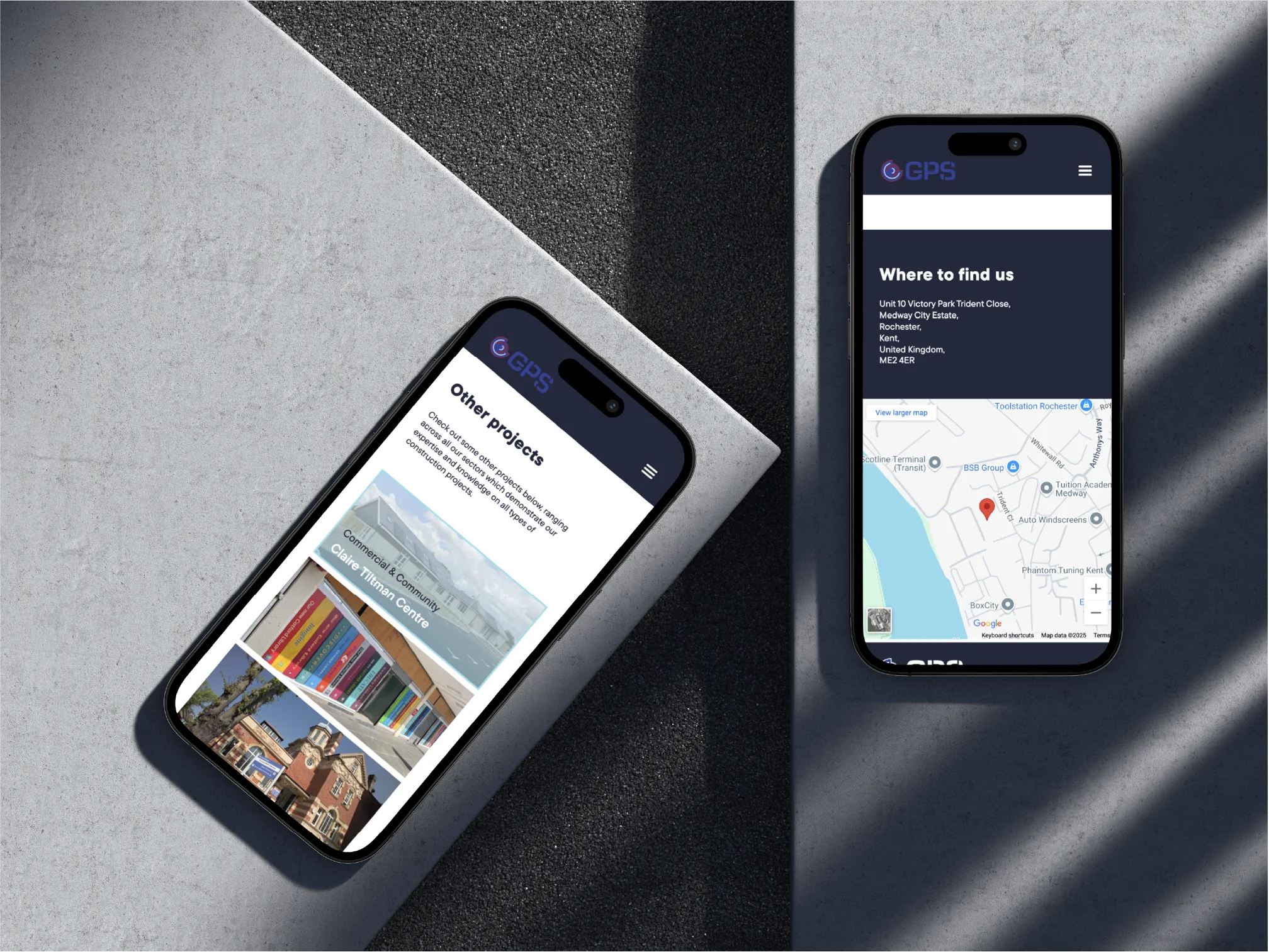 Two black smartphones on a textured surface displaying a GPS-related website, with one phone showing a 'Where to find us' section with a map and the other showing 'Other projects' with images of buildings.