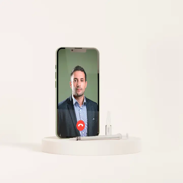 Imagem de um smartphone exibindo uma chamada de vídeo com Chris Airey. O telefone está posicionado verticalmente sobre uma plataforma circular branca, ao lado de uma seringa e uma ampola de medicamento. O fundo é completamente branco, dando destaque ao telefone e aos itens médicos.