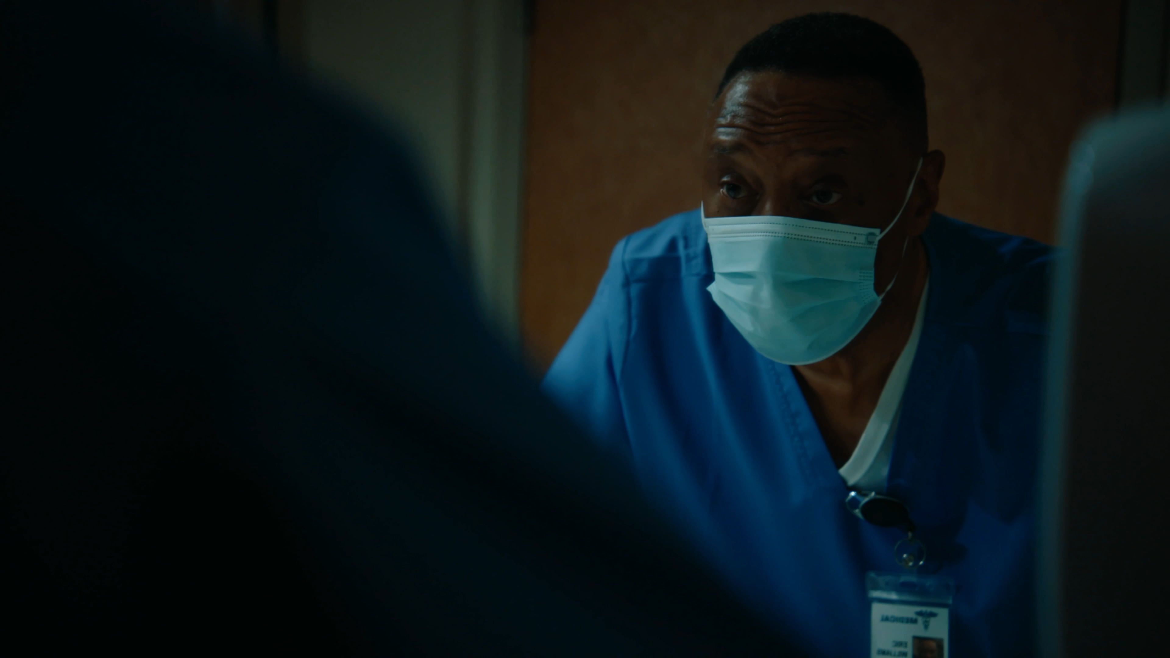 Certified nursing assistant in blue scrubs inside a hospital room