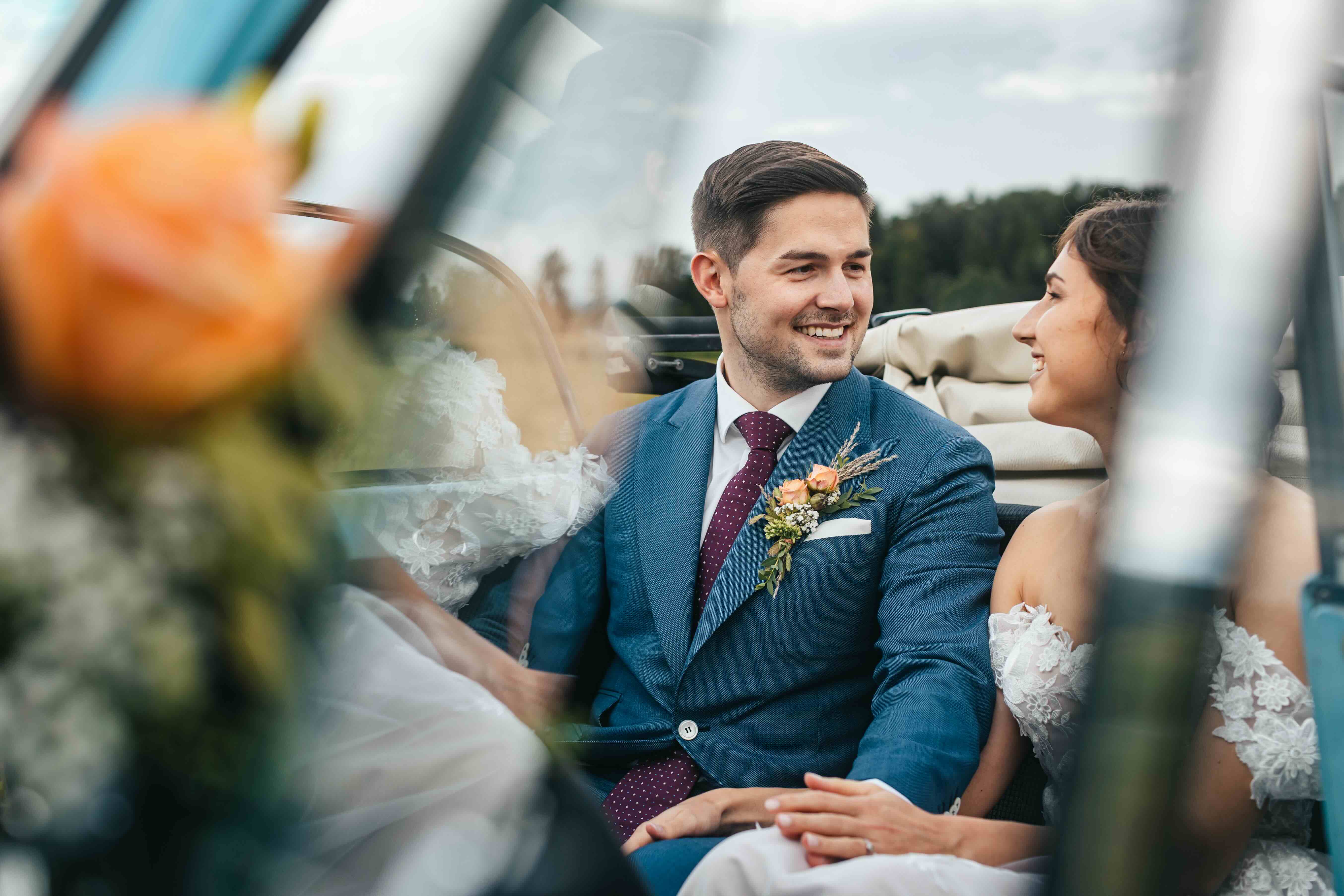 bride and groom sitting in a car with flowers in the back