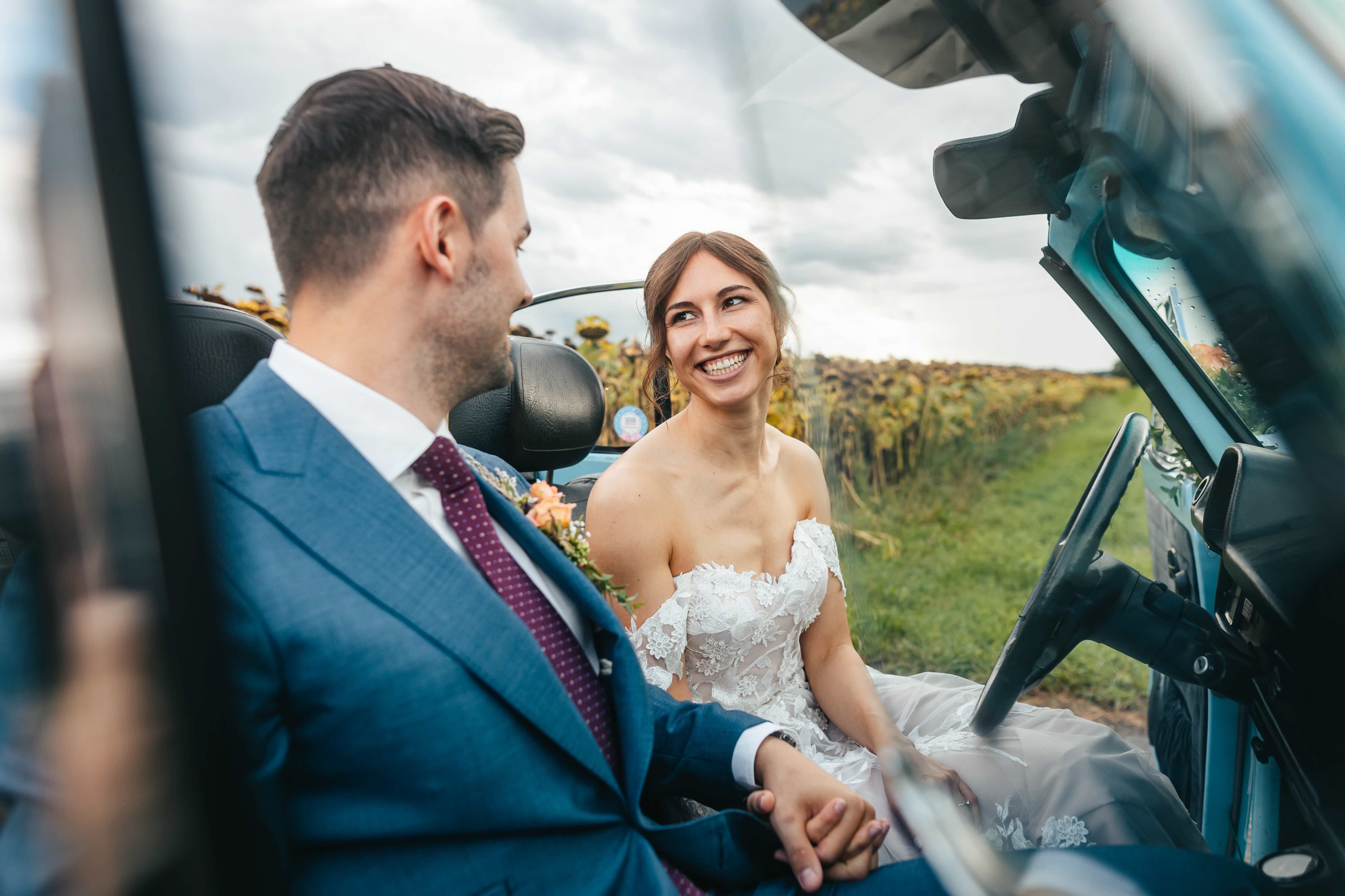 bride and groom sitting in a car smiling at each other