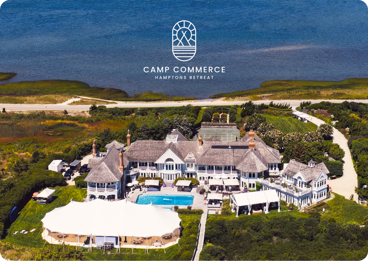 Aerial view of Camp Commerce Hamptons retreat with large house, pool, tents, and waterfront in background.