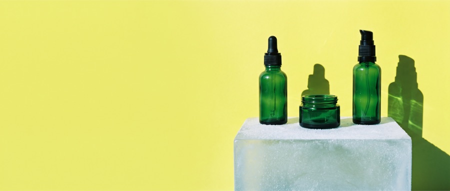 Green skincare bottles on a white plinth against yellow