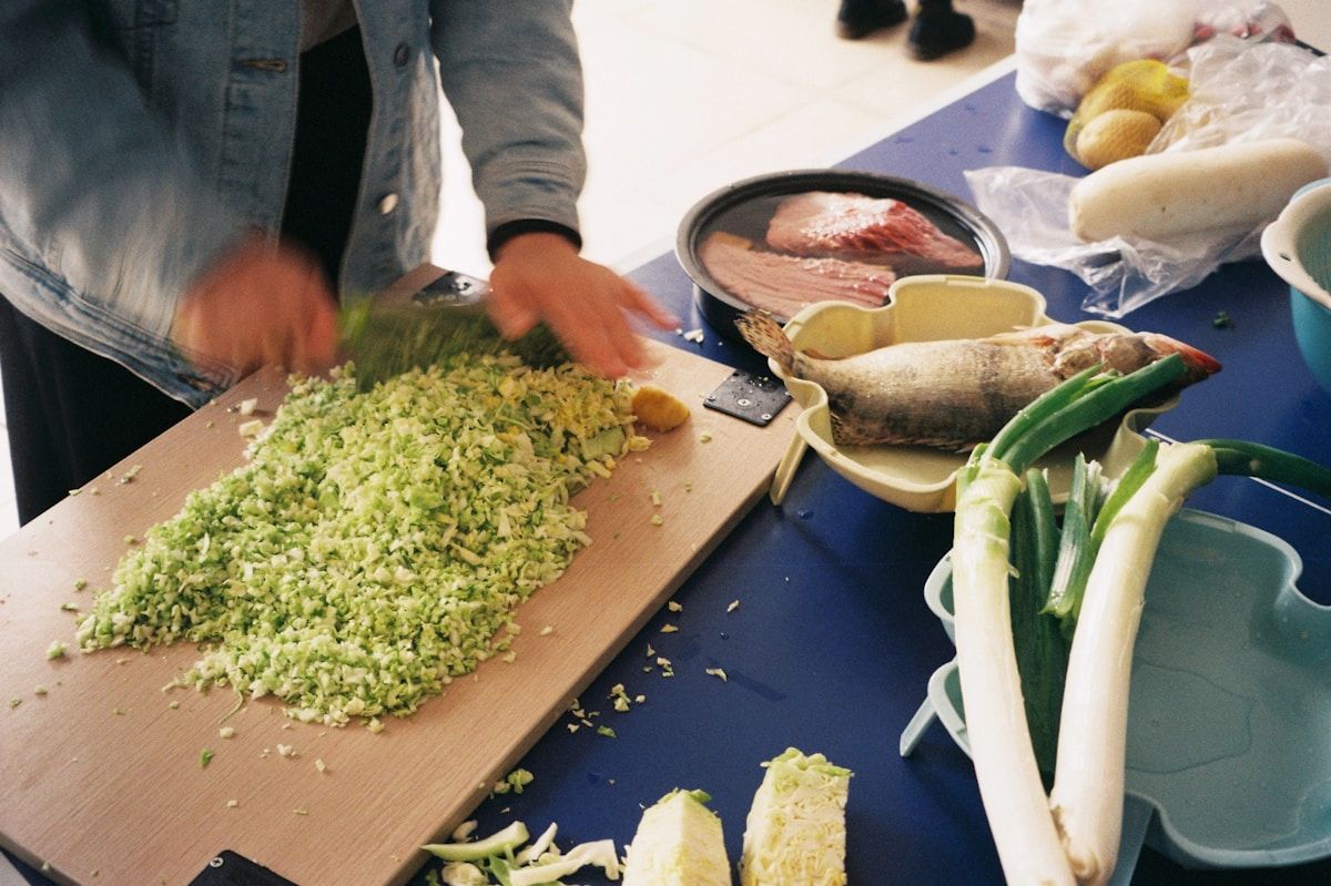 Person chopping fresh vegetables on a wooden cutting board.