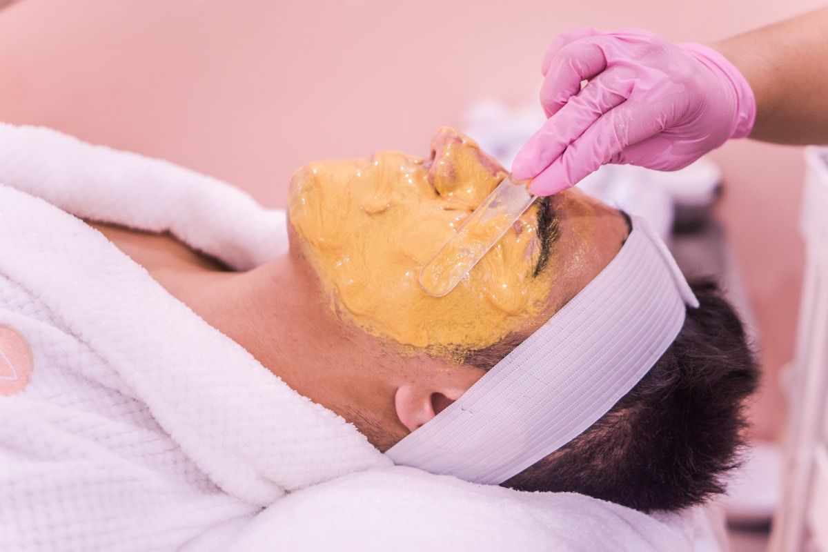 Masque facial jaune appliqué sur le visage d'une personne allongée sur une serviette blanche.