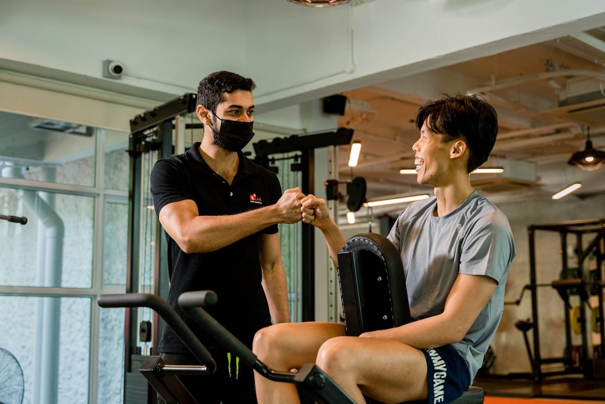 Deux hommes masqués dans une salle de gym, en train de discuter et de se serrer la main.