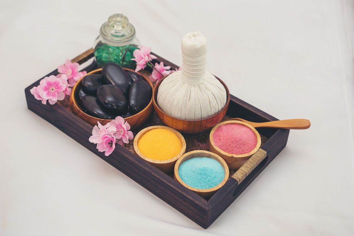 Plateau de produits de spa avec fleurs roses, pierres noires et poudres colorées.