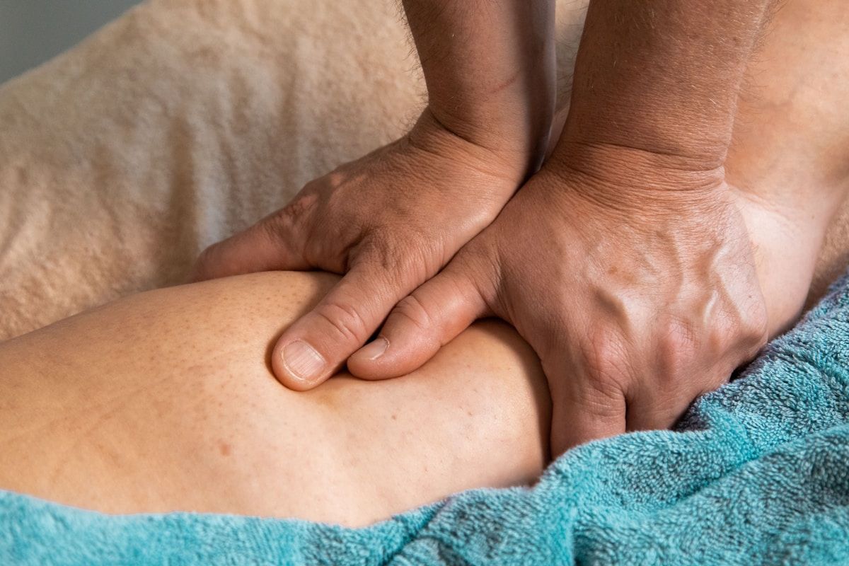 Mains massant délicatement une jambe enveloppée dans une serviette bleue.