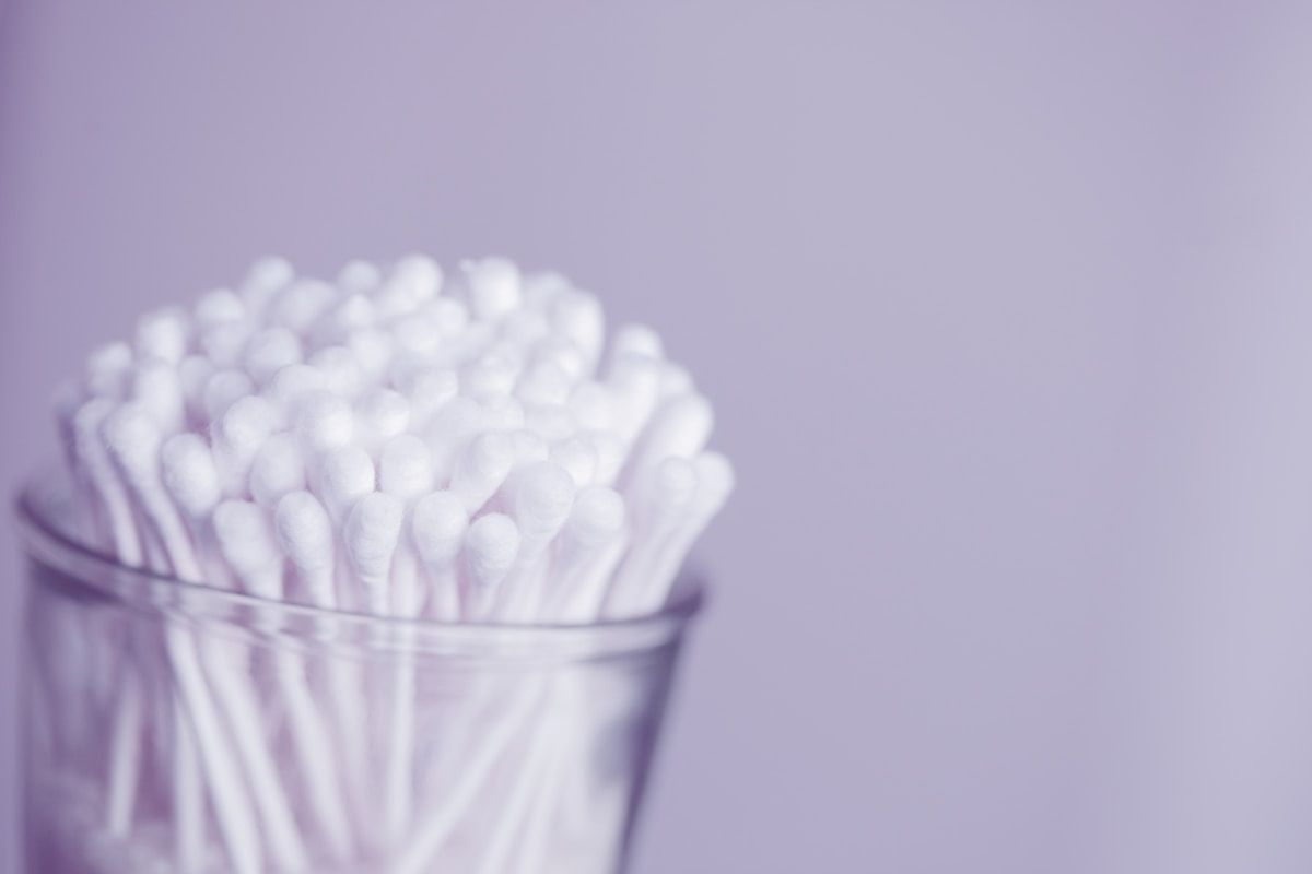 Coton-tiges blancs dans un verre transparent sur fond violet.