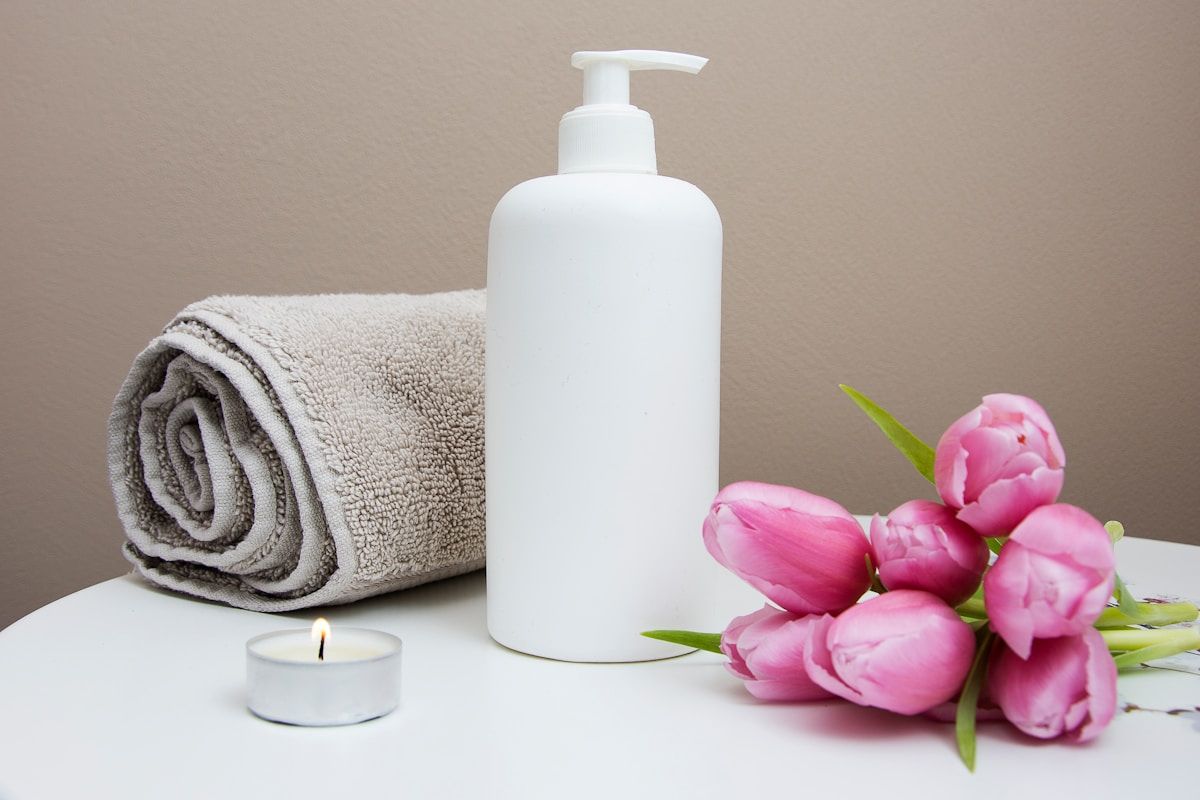 Serviette enroulée, bouteille de lotion, tulipes roses, bougie allumée.