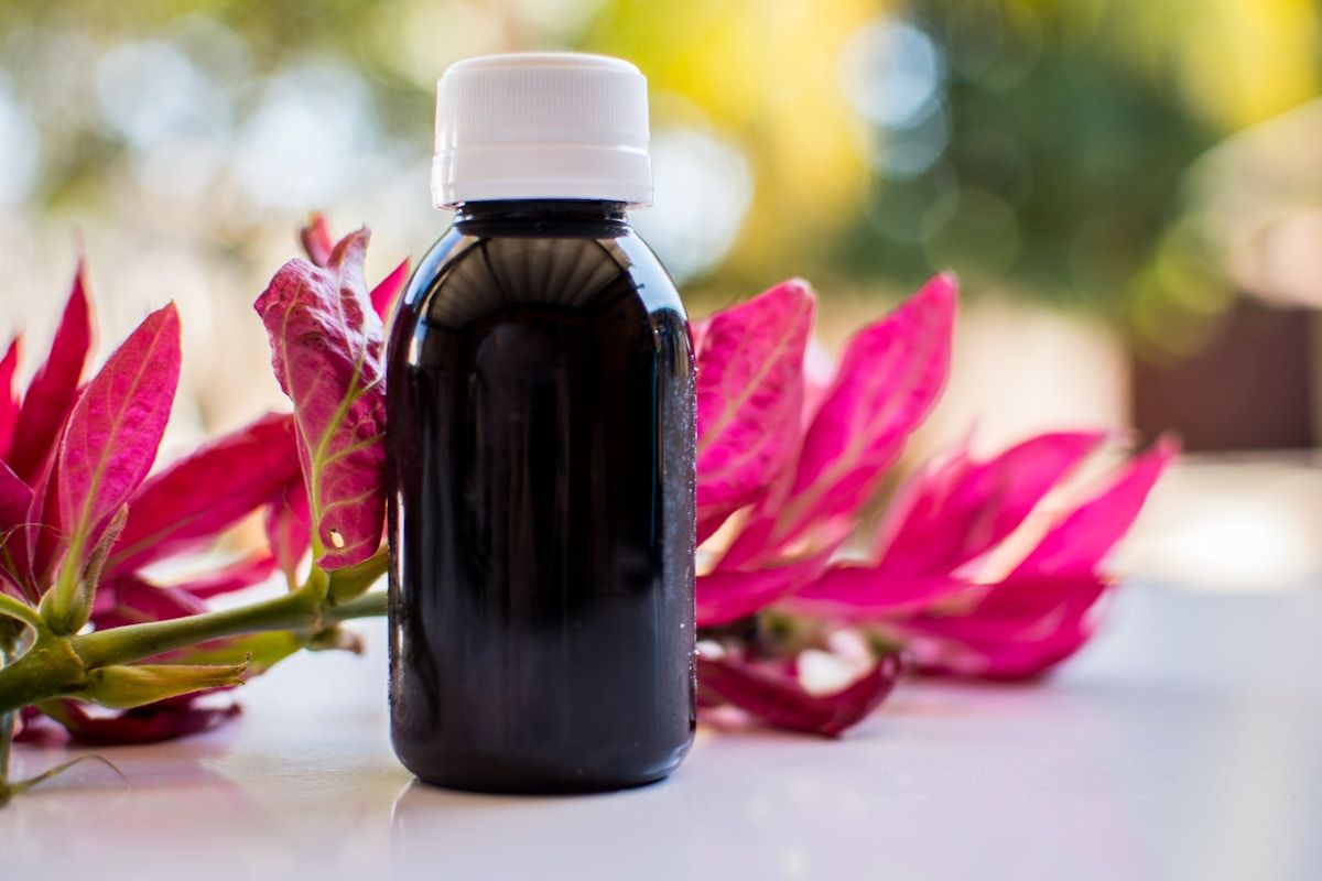 Bouteille noire de produit naturel entourée de fleurs rouges.