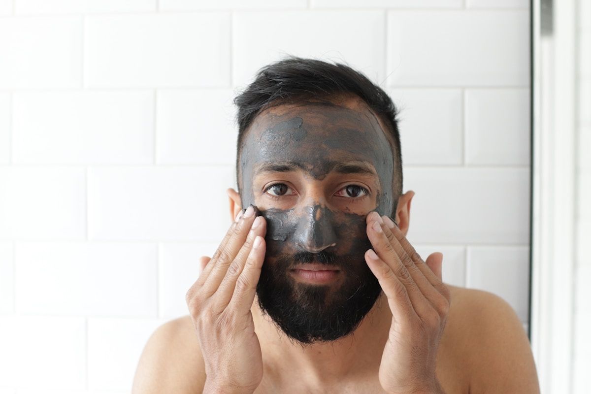 Homme appliquant un masque facial noir sur son visage barbu.