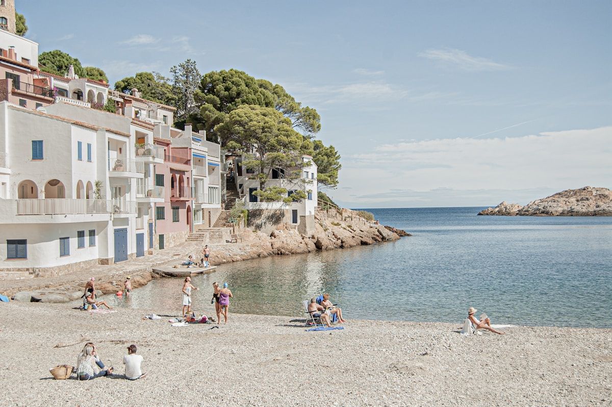 Plage méditerranéenne bordée de maisons colorées, avec des vacanciers profitant du soleil.