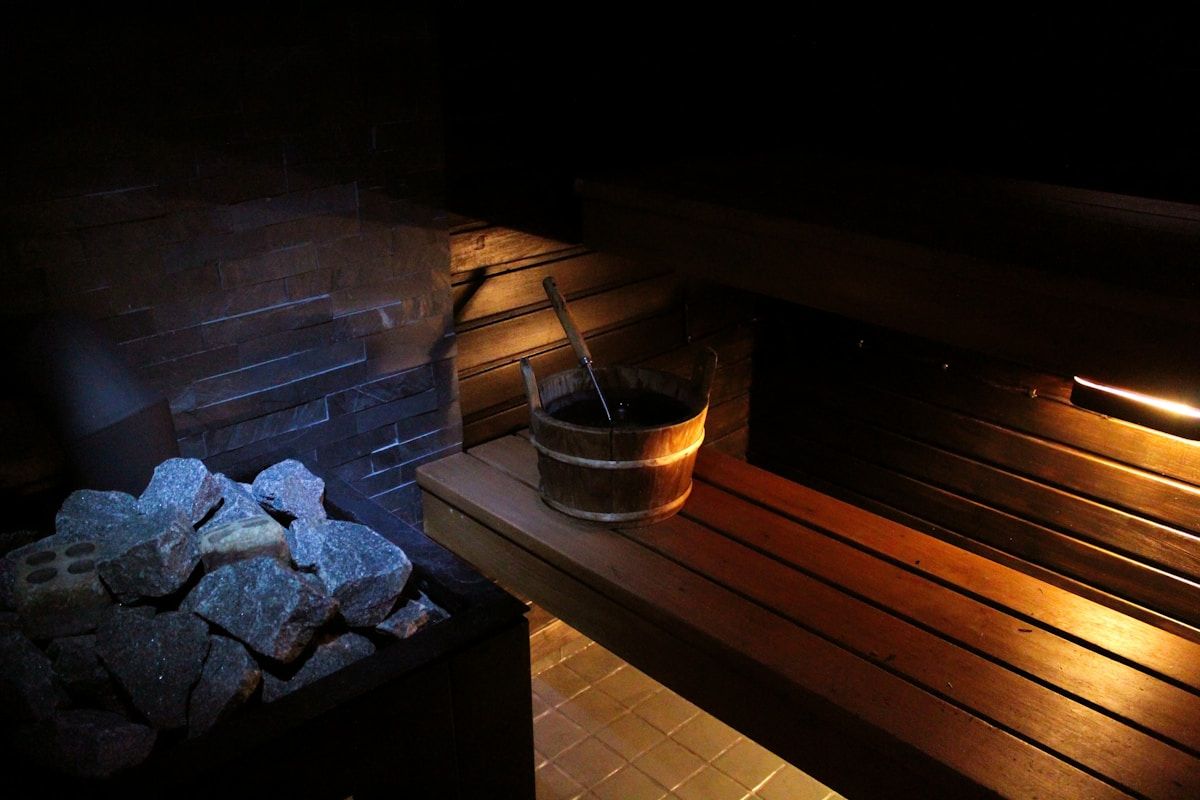 Sauna en bois sombre avec pierres chauffées et seau en bois.