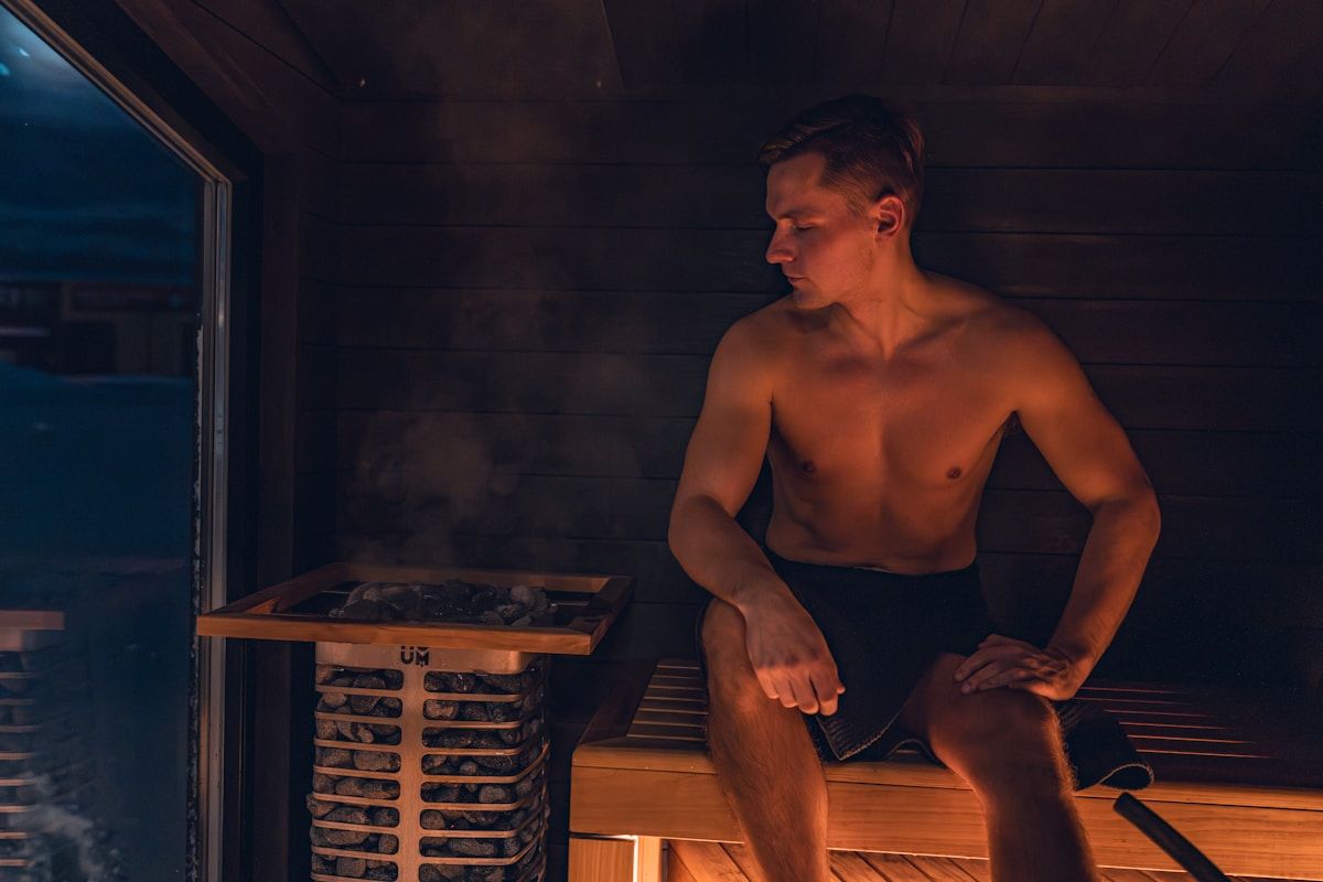 Homme torse nu assis dans un sauna, éclairé par une lumière bleutée.