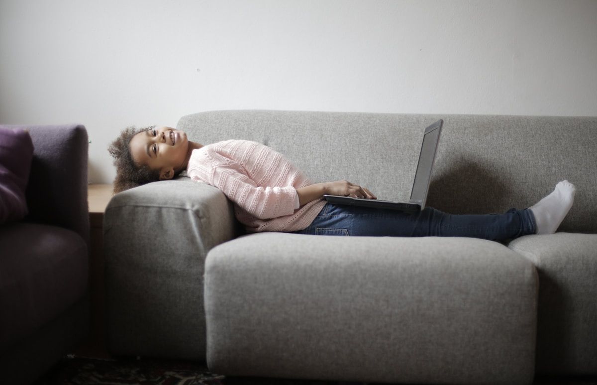 Femme allongée sur un canapé avec un ordinateur portable.