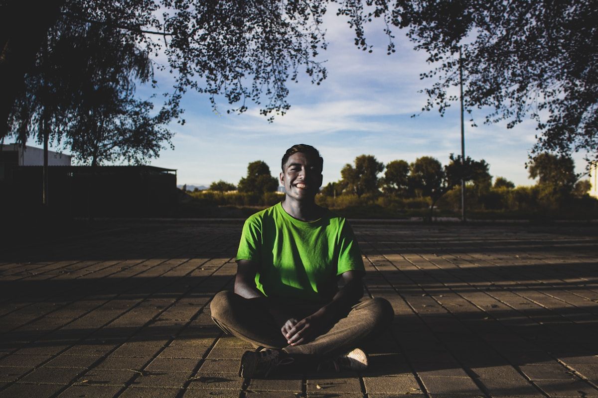 Jeune homme souriant assis sur un sol en brique dans un parc.