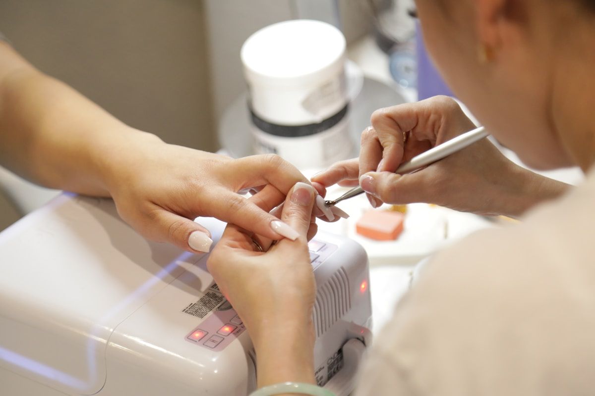 Mains de manucure effectuant un traitement des ongles avec un appareil électrique.