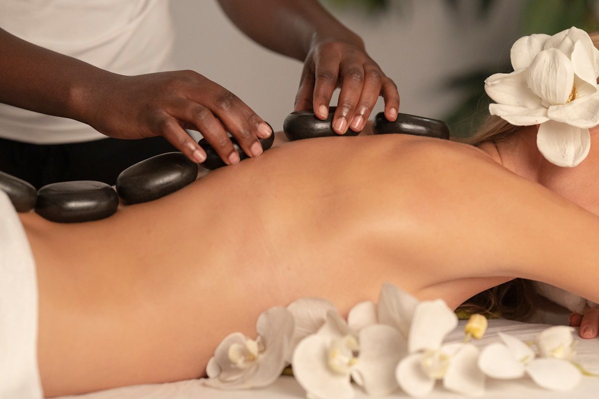 Massage thérapeutique avec pierres chaudes et fleurs blanches.