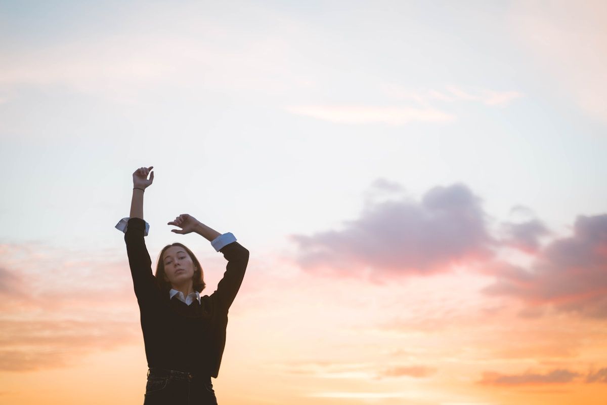 Une femme levant les bras au coucher de soleil.