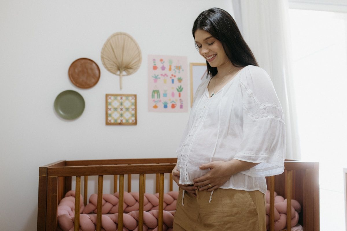 Femme enceinte souriante dans une chambre d'enfant décorée.