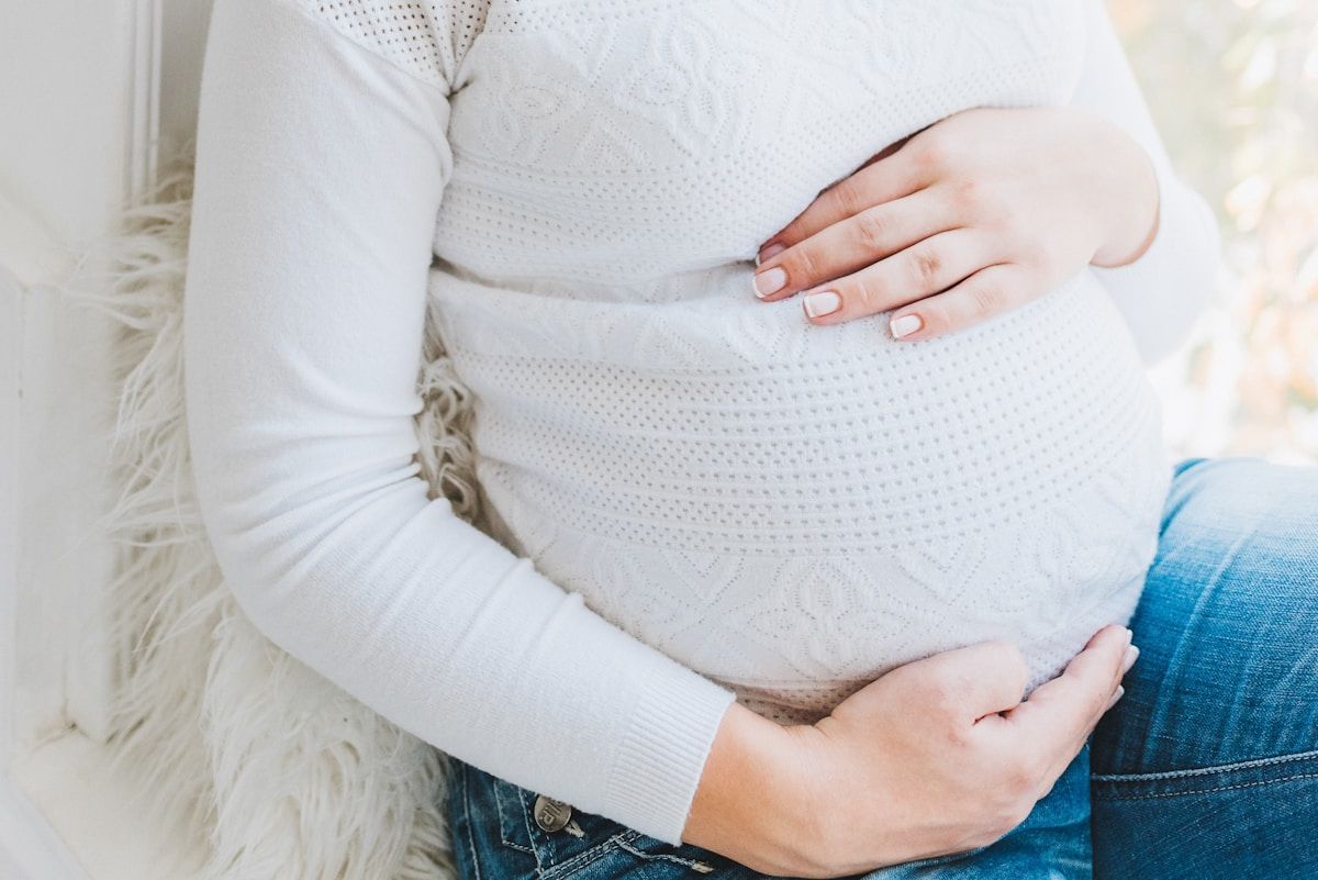 Femme enceinte dans un pull blanc, mains sur le ventre.