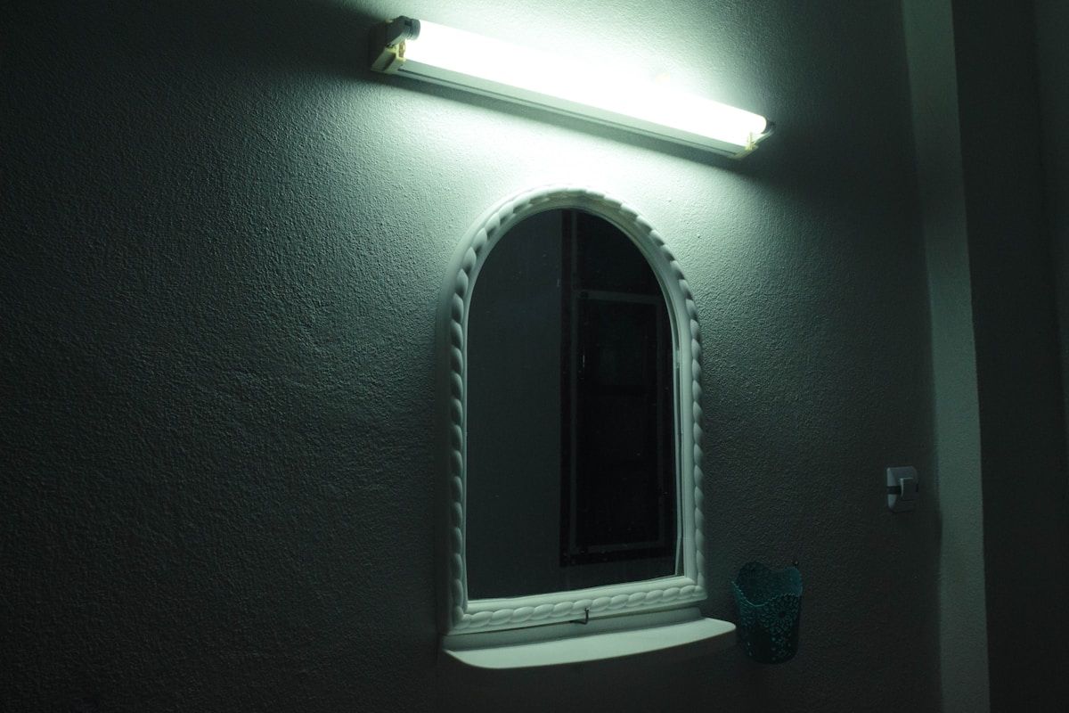 Miroir décoratif ovale sur mur sombre, éclairé par lampe.
