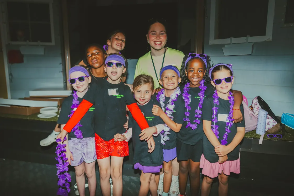 Summer Fest kids in purple boas and sunglasses posing with a leader at check-in