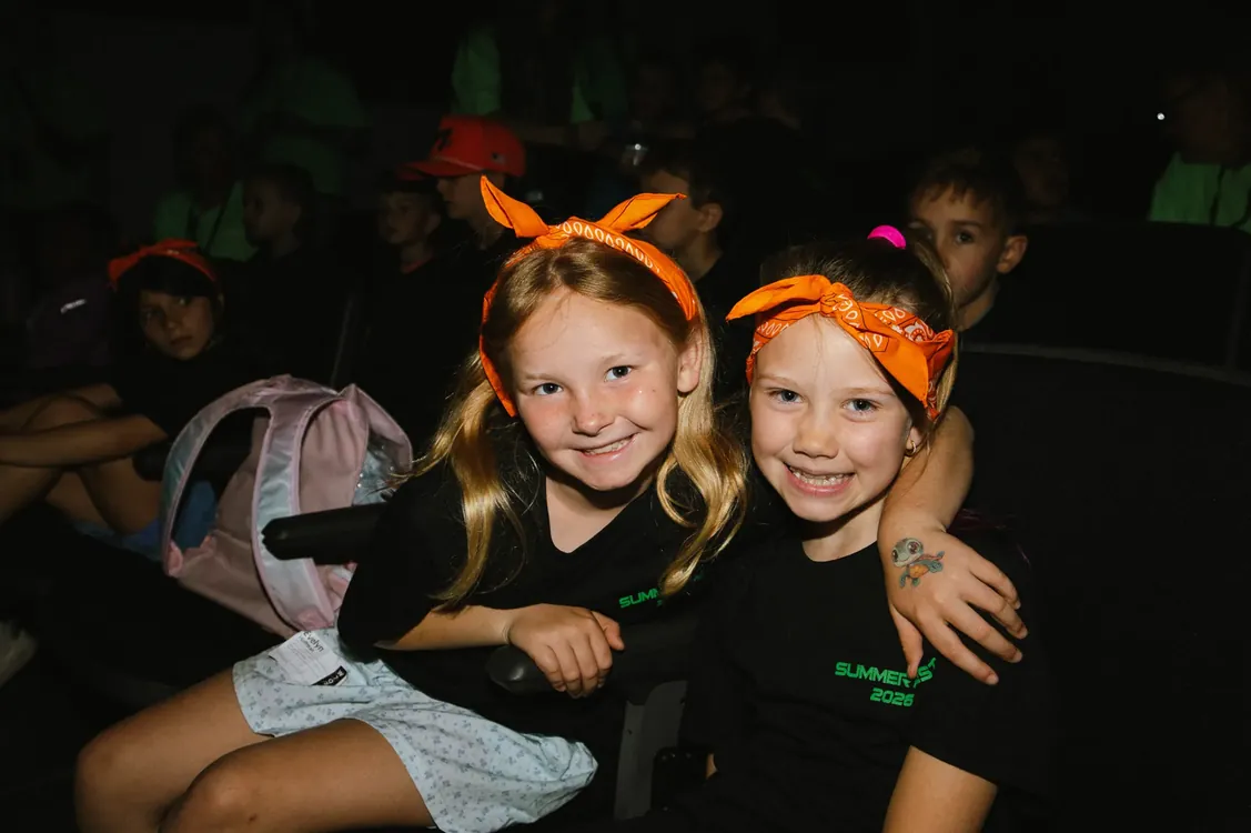Two girls in orange bandanas smiling in the auditorium