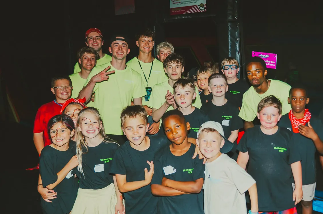 Leaders and kids posing together under neon lights
