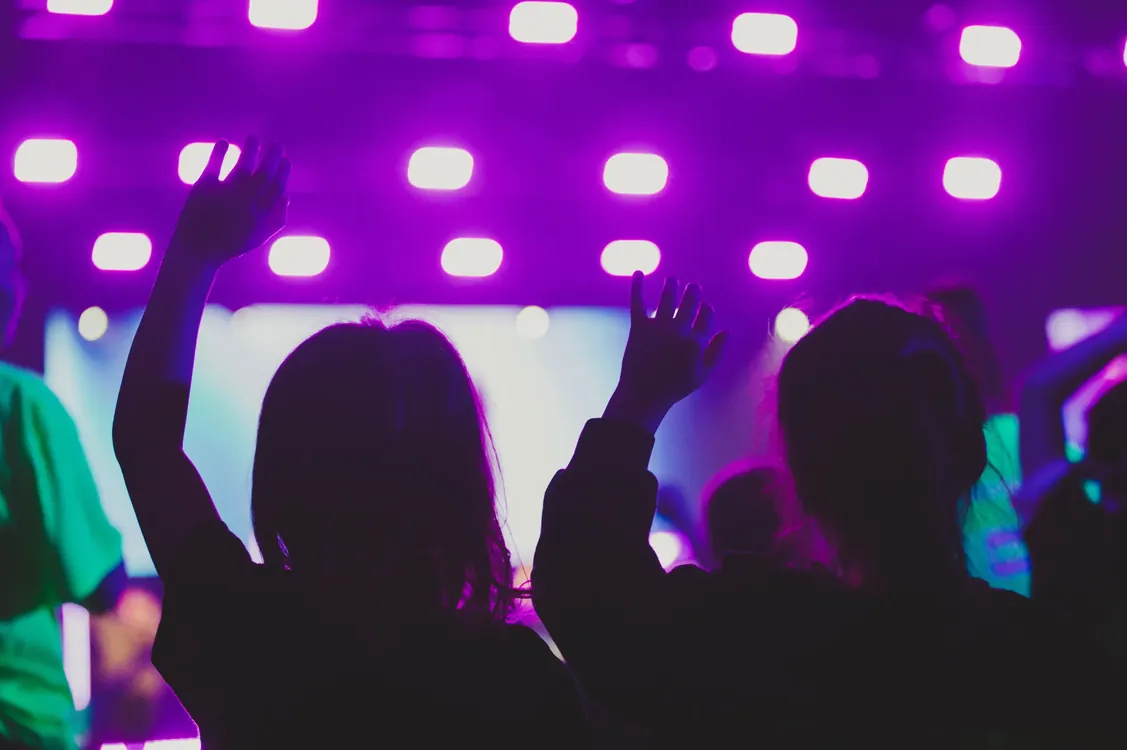 Kids raising their hands in worship under purple lights
