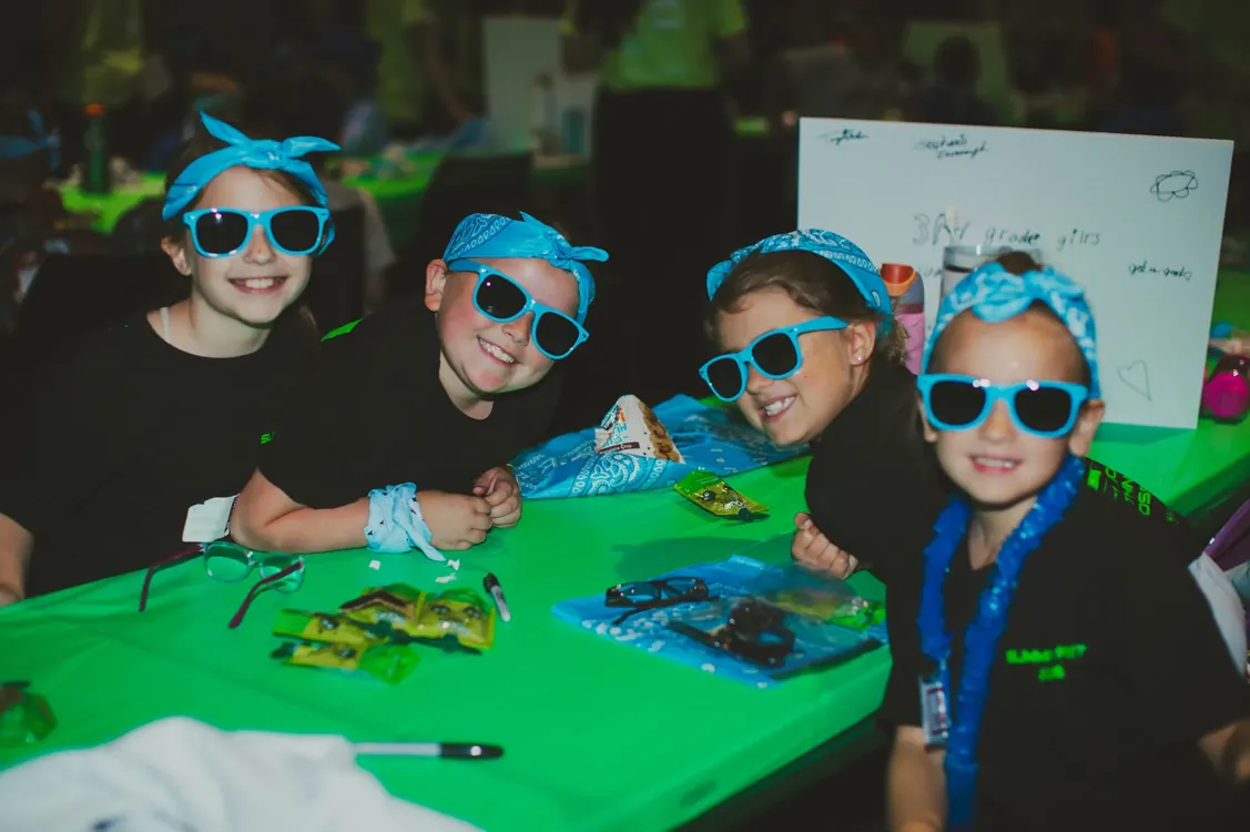 Kids in blue bandanas and sunglasses at a craft table