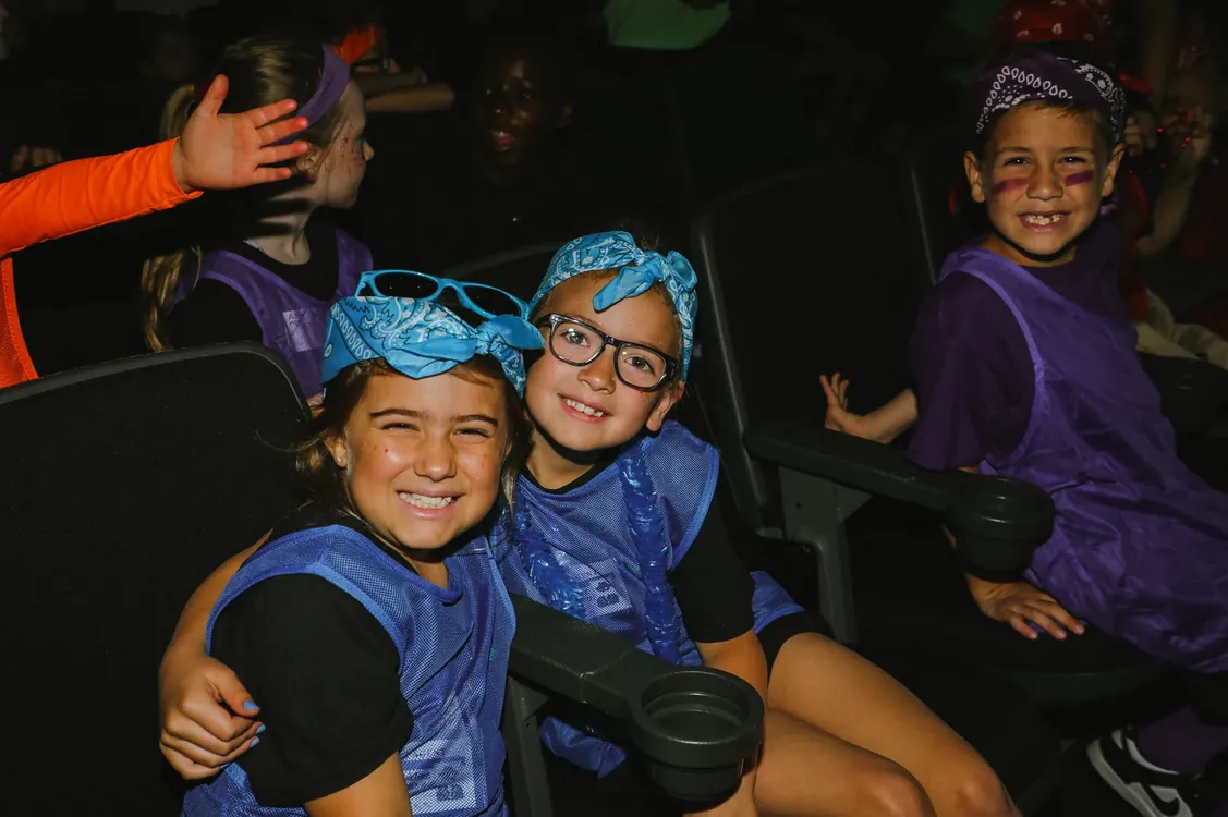 Kids in blue bandanas smiling in the auditorium seats