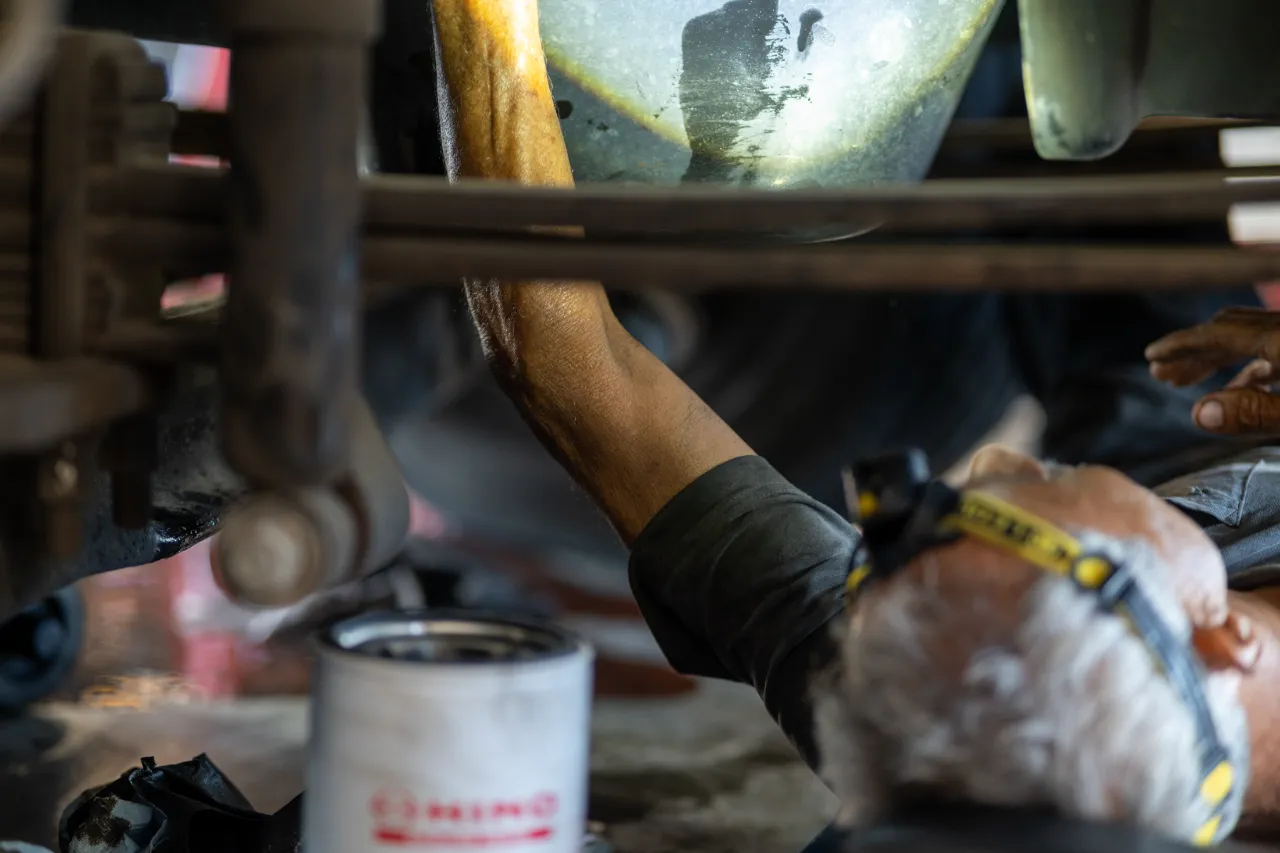 Technician performs an oil filter service under a heavy-duty vehicle with a KING brand filter nearby.