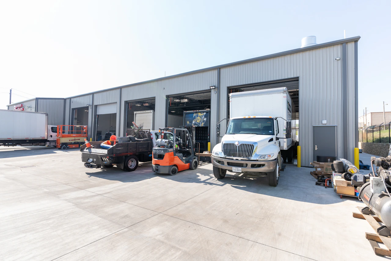 Heavy-duty repair shop with service bays, a box truck, forklift, and work vehicles outside the facility.