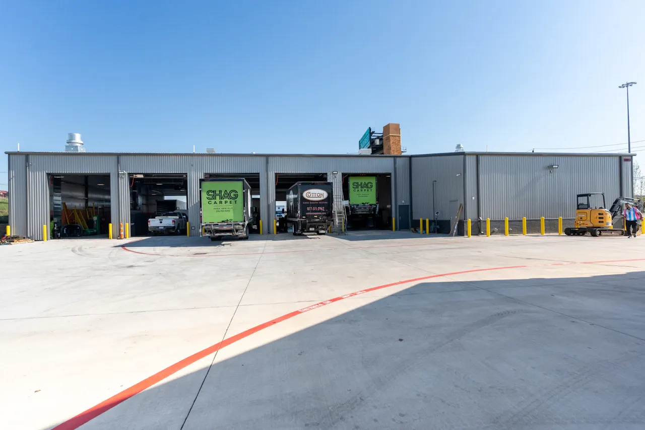 Heavy-duty repair facility with multiple service bays and commercial trucks undergoing maintenance. Trailer doors display "SHAG CARPET" and "GITON."