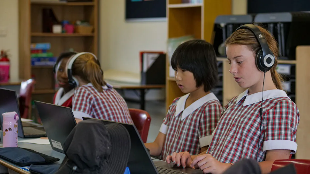 A girl wearing headphones and a red and white dress is using a laptop.