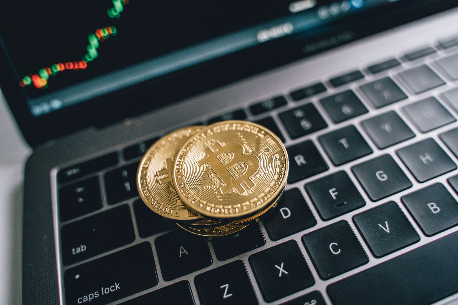 Gold bitcoin coins resting on a laptop keyboard with a trading chart on screen
