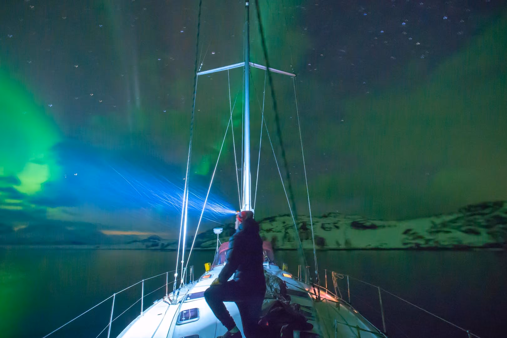 Sailboat mast outlined against a bright green northern lights sky.