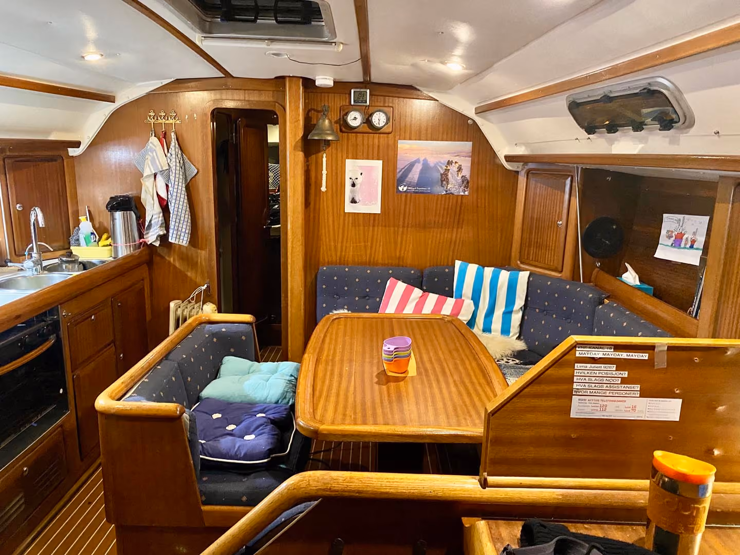 Cozy boat cabin with wood interior, dining table, cushioned seating, kitchen sink, and hanging towels.