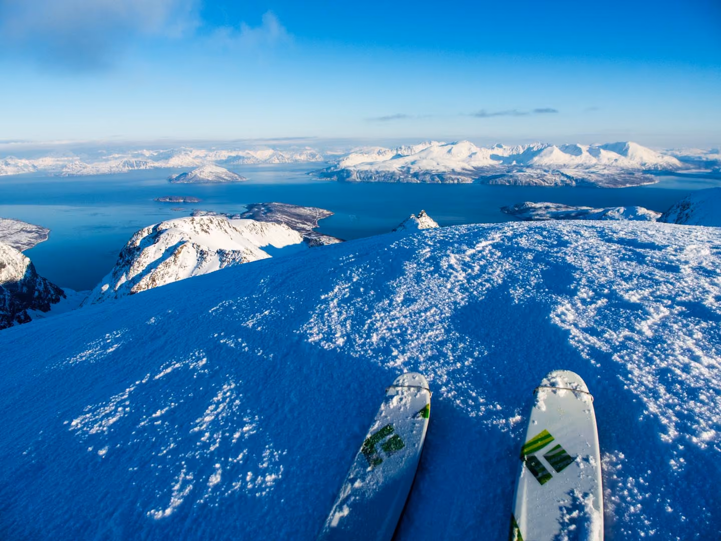 Looking down a steep snowy mountain slope toward deep blue ocean waters.