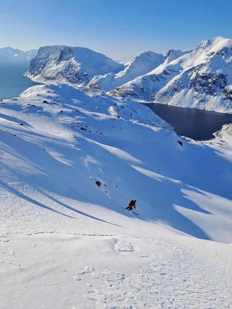 Skier descending a snow slope with jagged mountain peaks in the background.