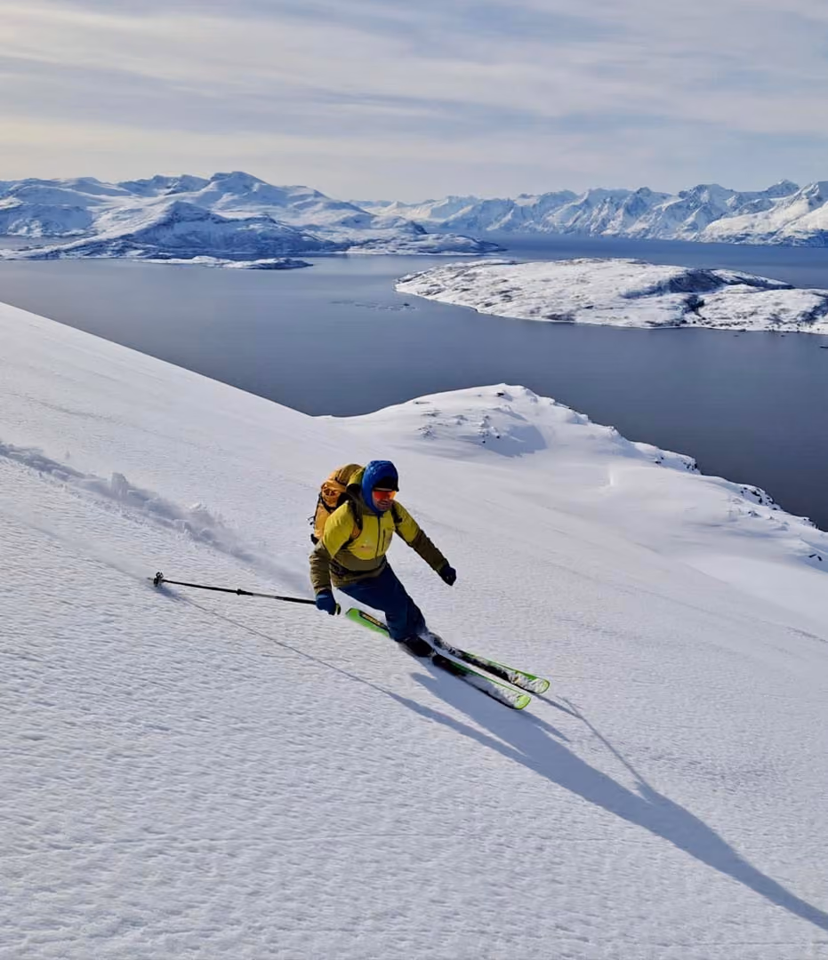Skier carving down a pristine, snow-covered mountain slope facing the sea.