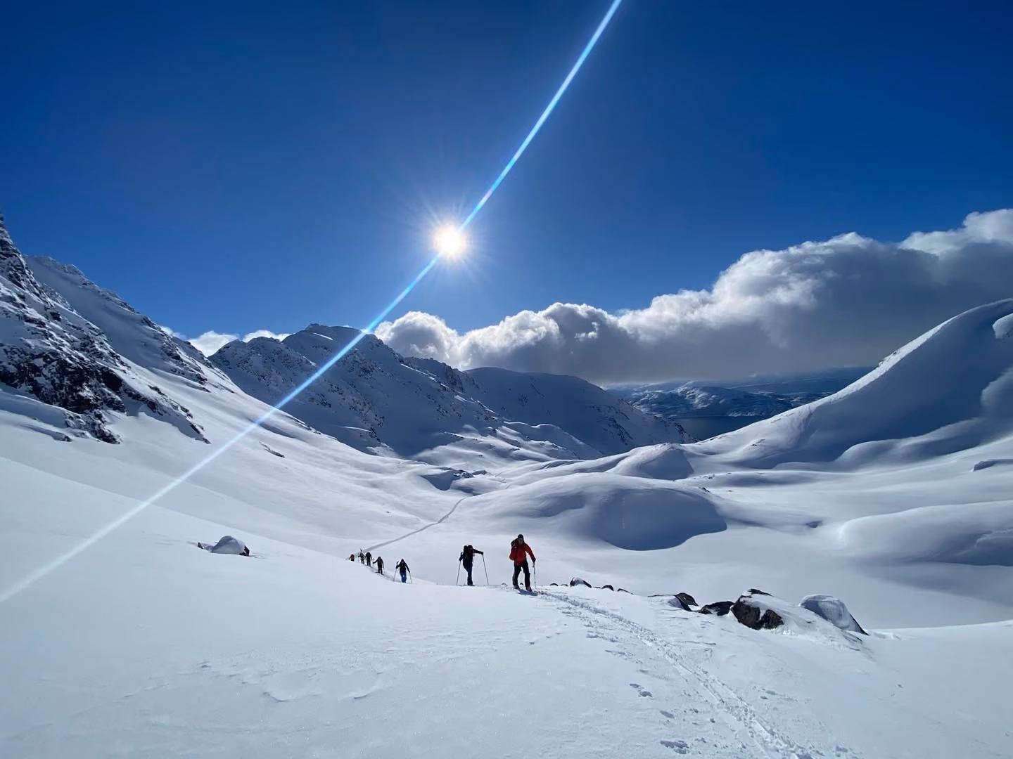 Skiers ascending a wide snowfield under a bright, sunny sky.