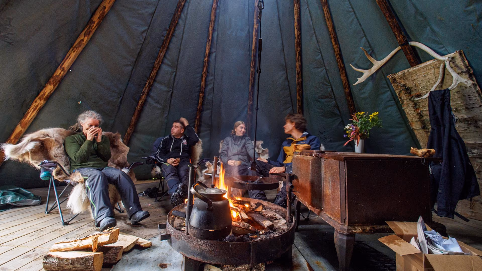 Group of people sitting around a campfire inside a traditional lavvu tent.