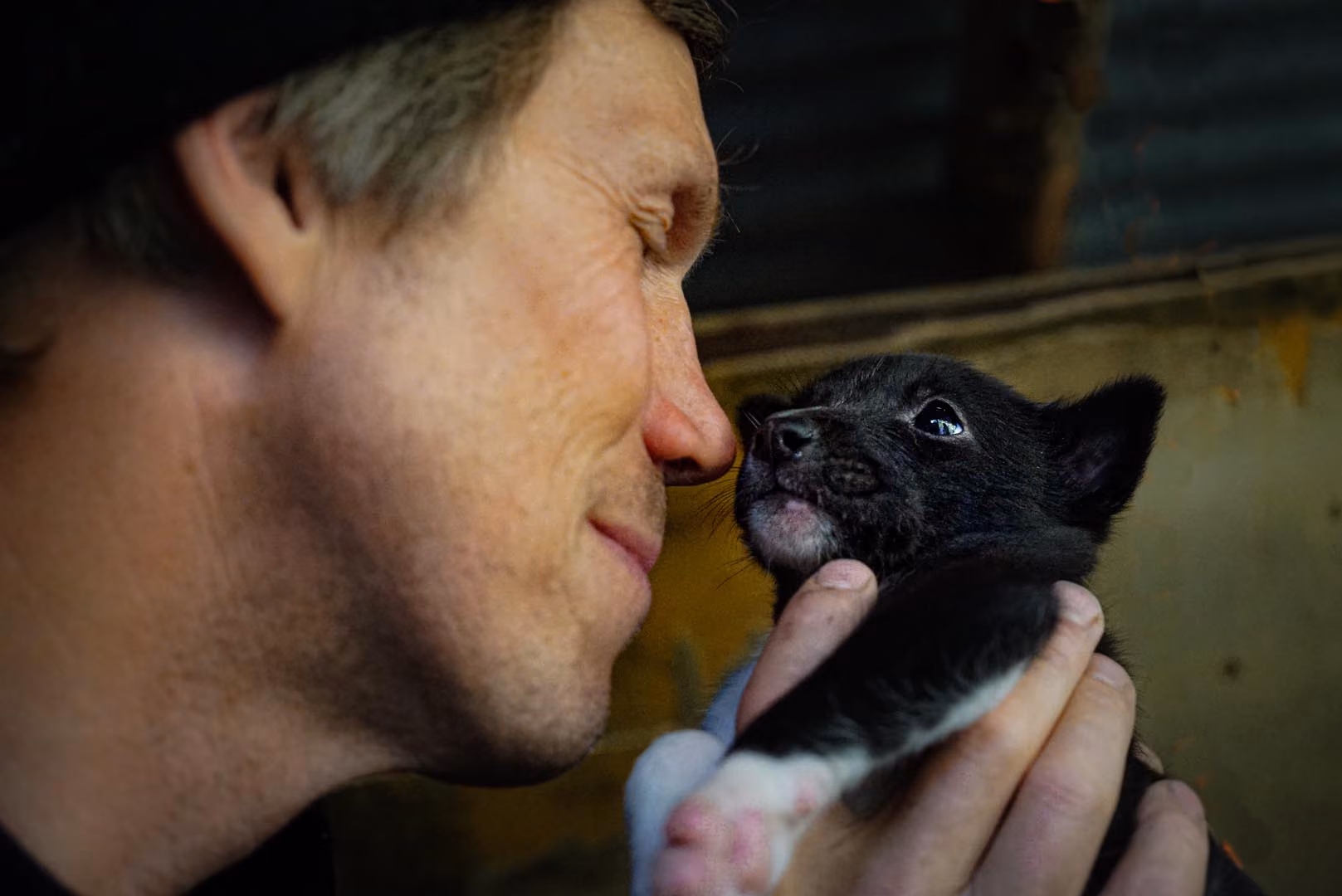 Man holding a small black puppy close to his face.