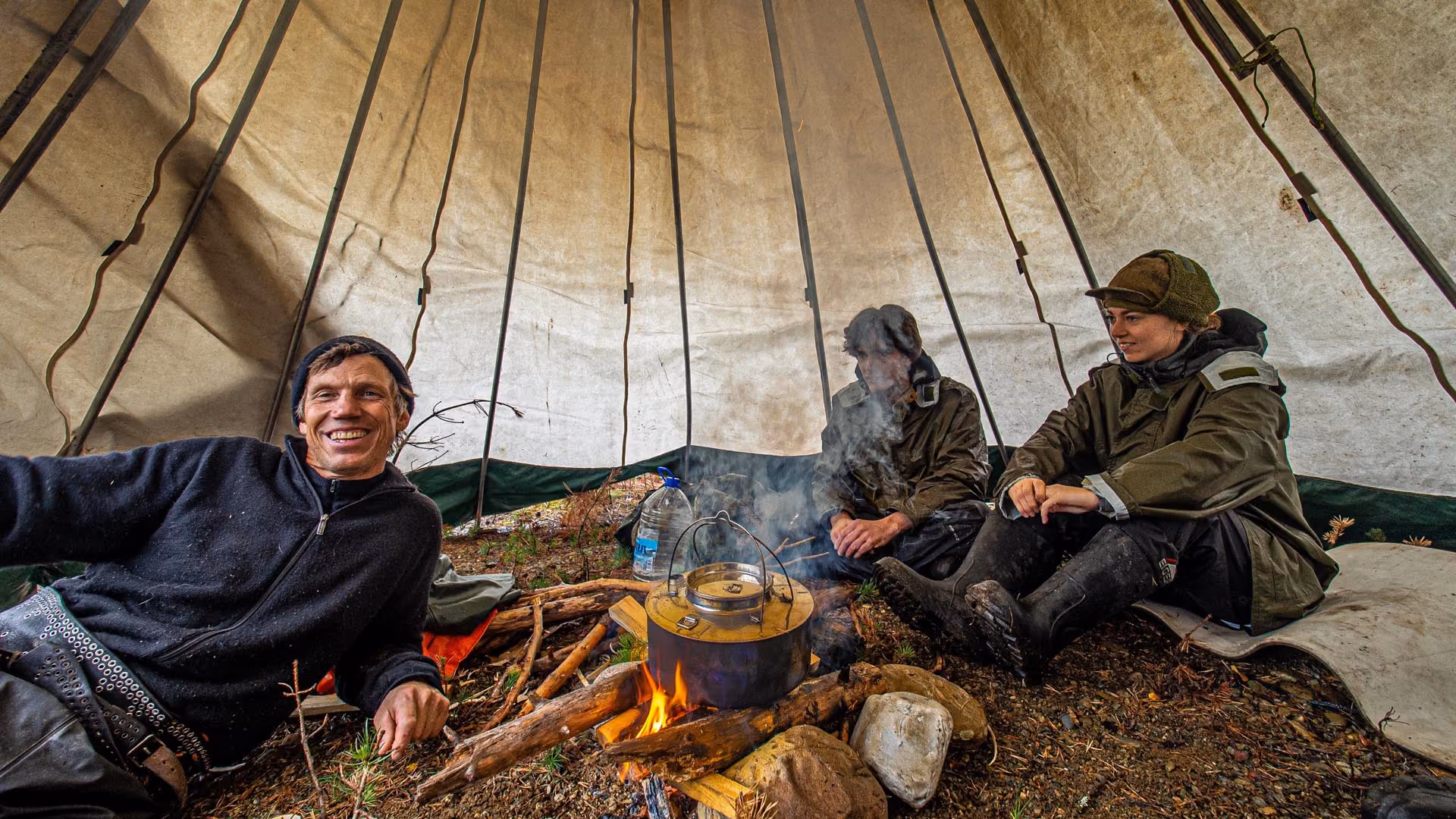 People relaxing inside a lavvu tent around a warm central fire.