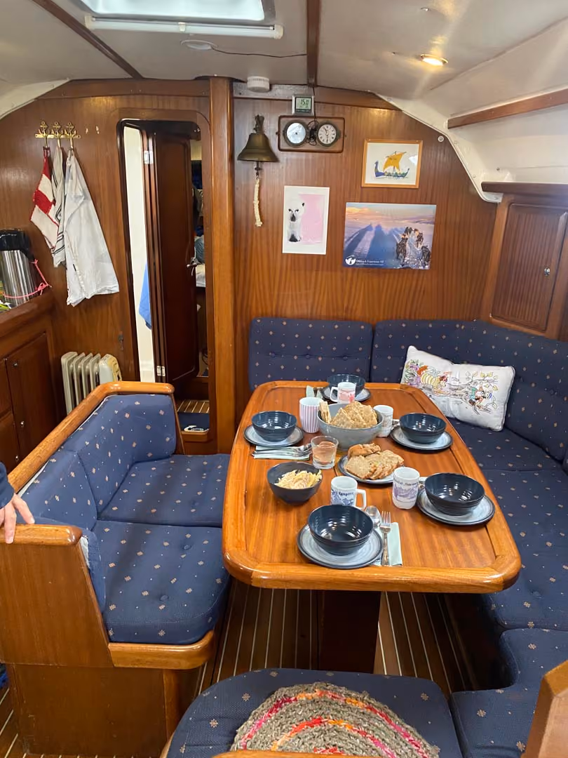 Interior of a sailboat cabin with blue seating and a set wooden dining table.