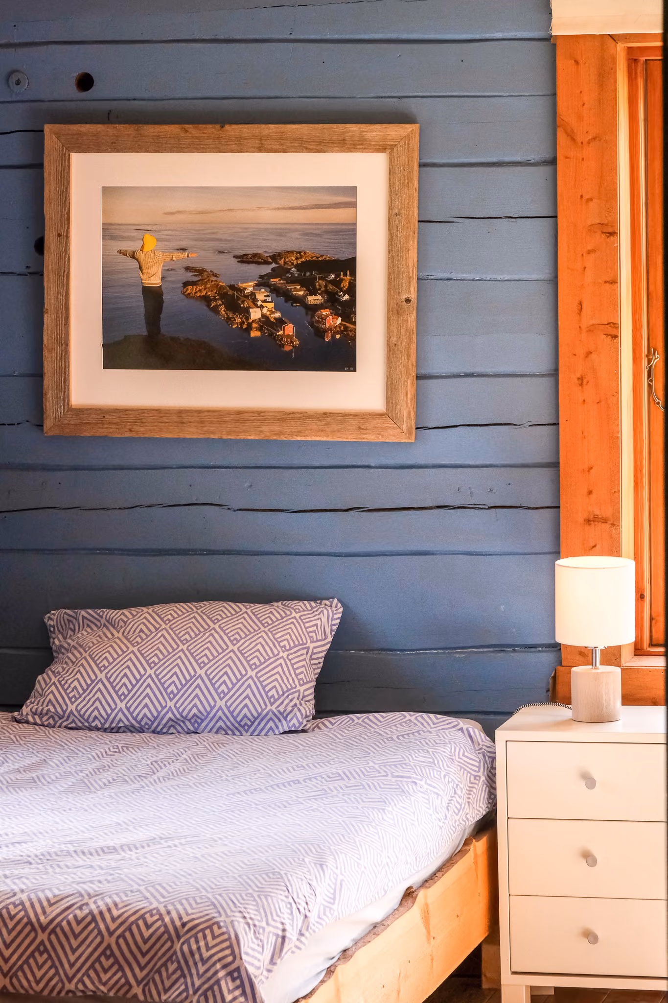 Bedroom with a single bed and a framed picture on a blue paneled wall.