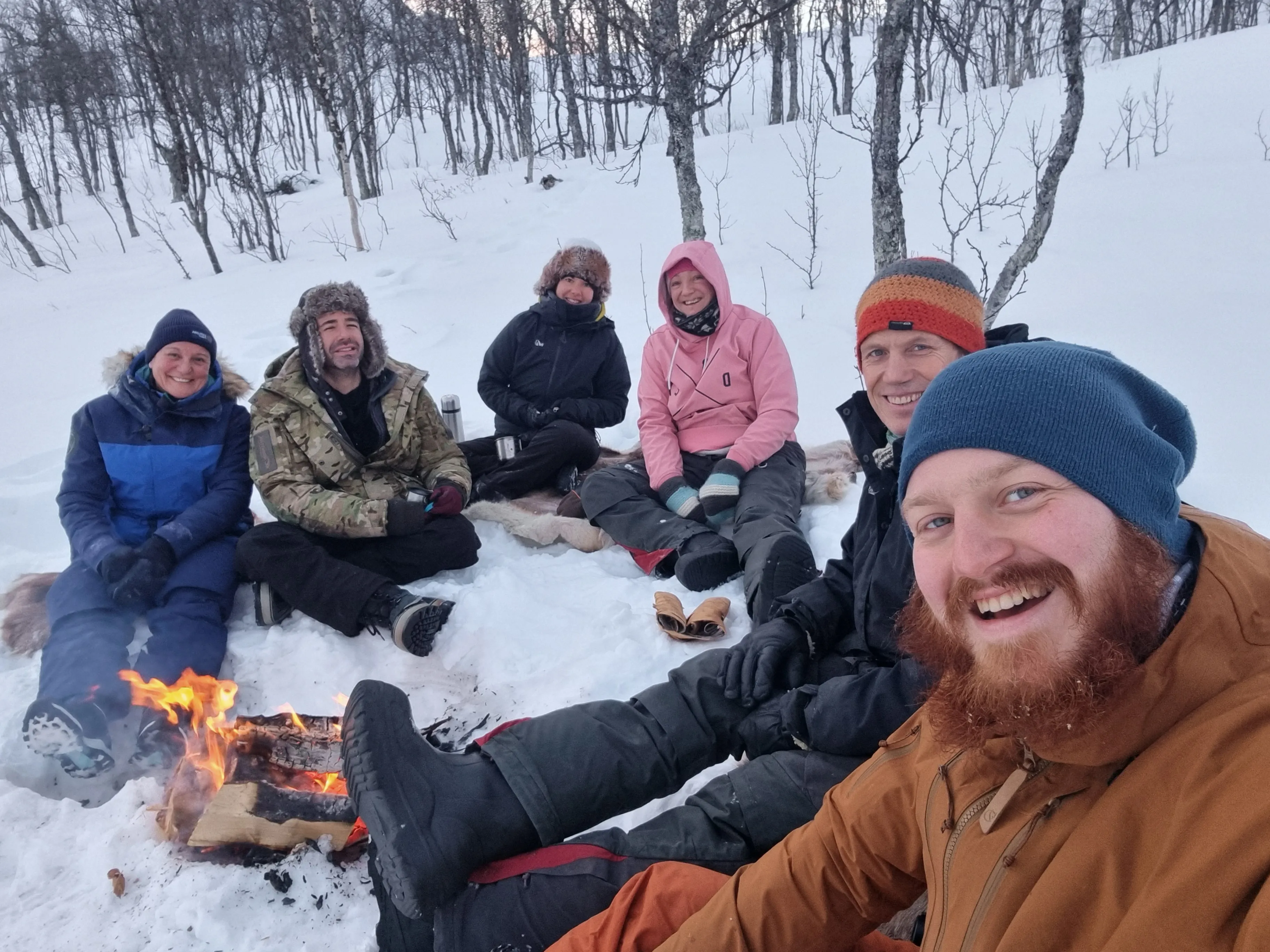 A group of people gather around a campfire in the snow.